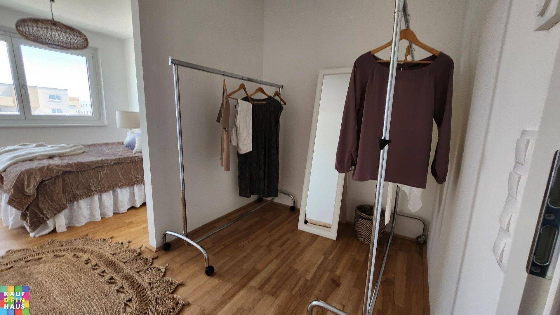Schlafzimmer mit Holzboden, Fenster und einem mobilen Kleiderständer.