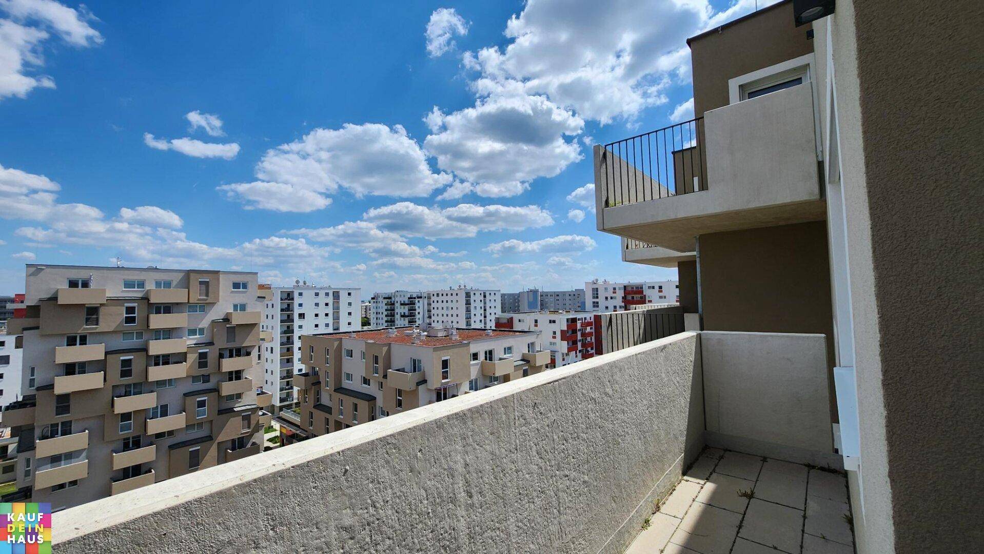 Balkon mit Stadtblick und umliegenden Wohngebäuden unter blauem Himmel.