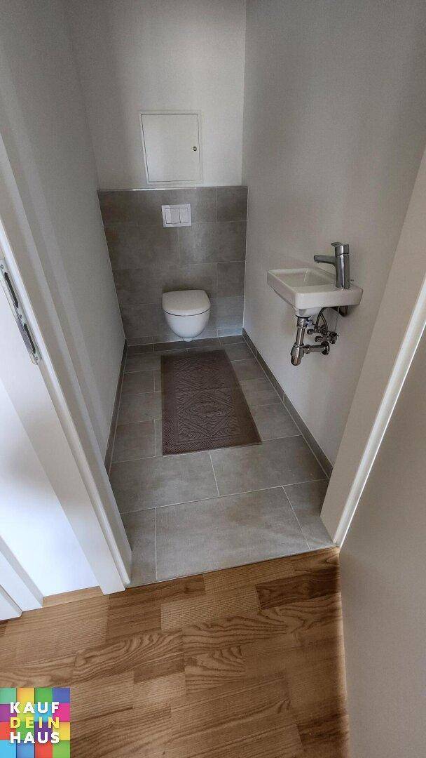 Kleines Gäste-WC mit Wand-WC, Waschbecken und modernen Fliesen.