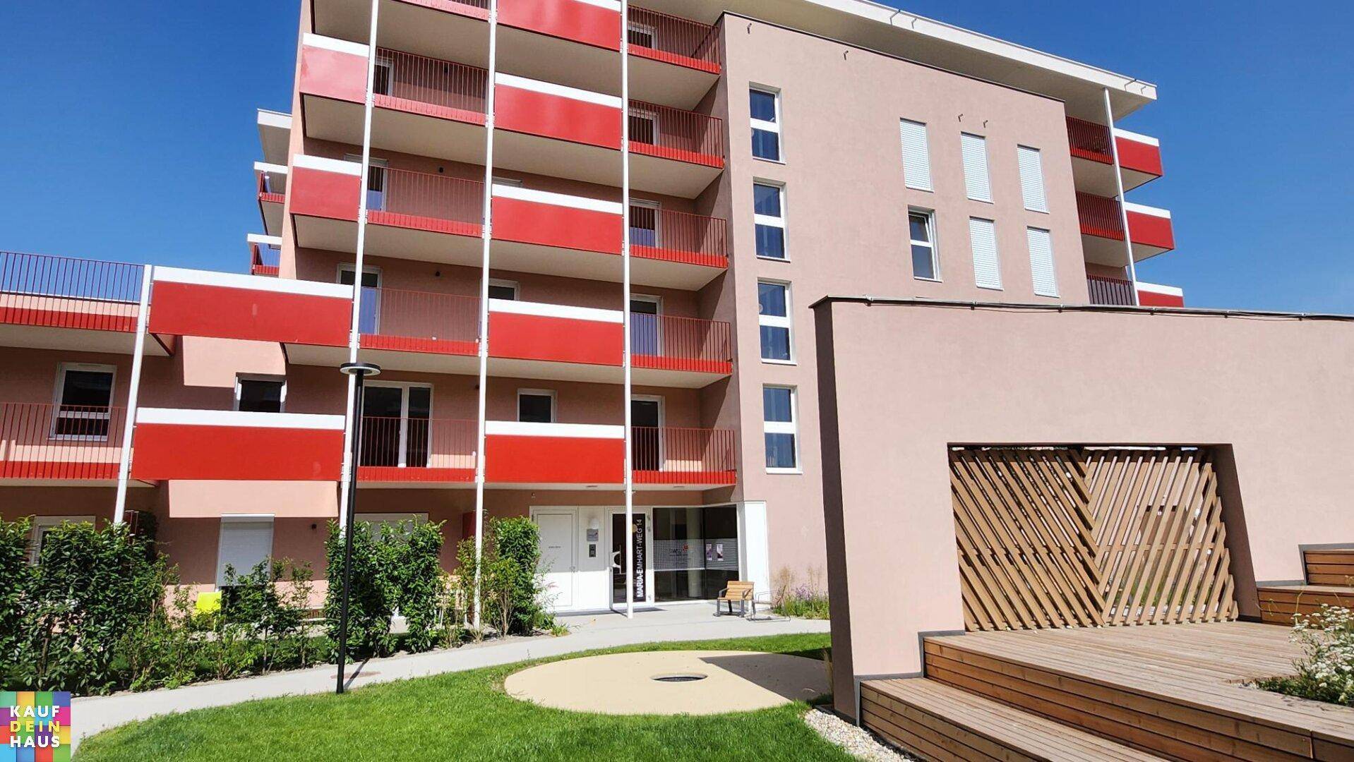 Eingangsbereich eines modernen Wohngebäudes mit roter Balkonfassade und Holzdetails.