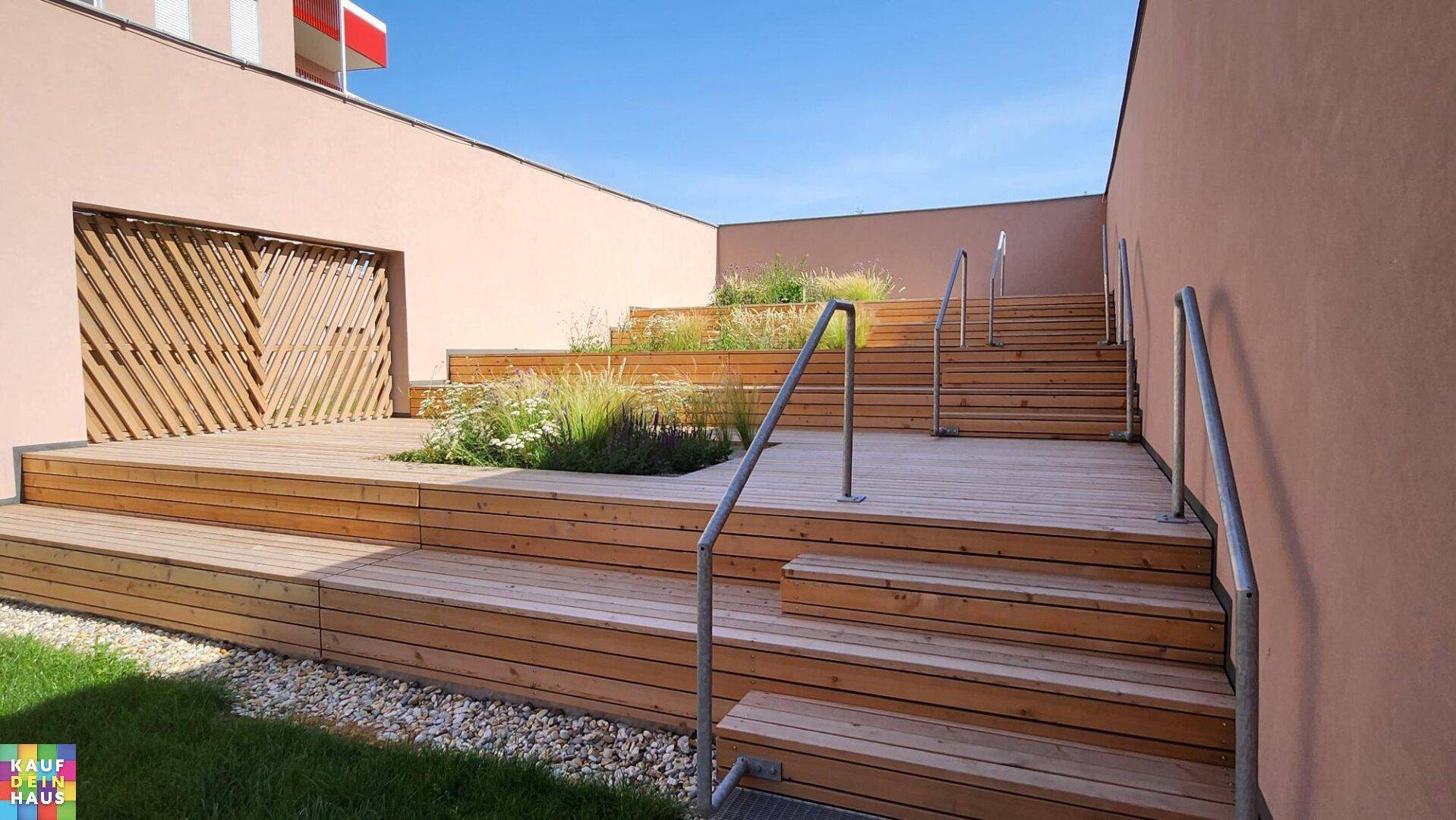 Gestufte Holzterrasse mit Metallgeländern und integrierten Pflanzbeeten in der Außenanlage.