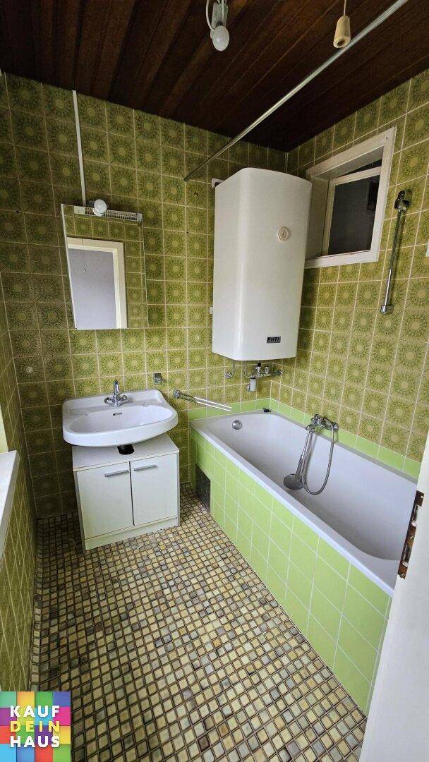 Badezimmer mit grünen Fliesen, Badewanne, Waschbecken und Fenster, im Stil der 80er Jahre.