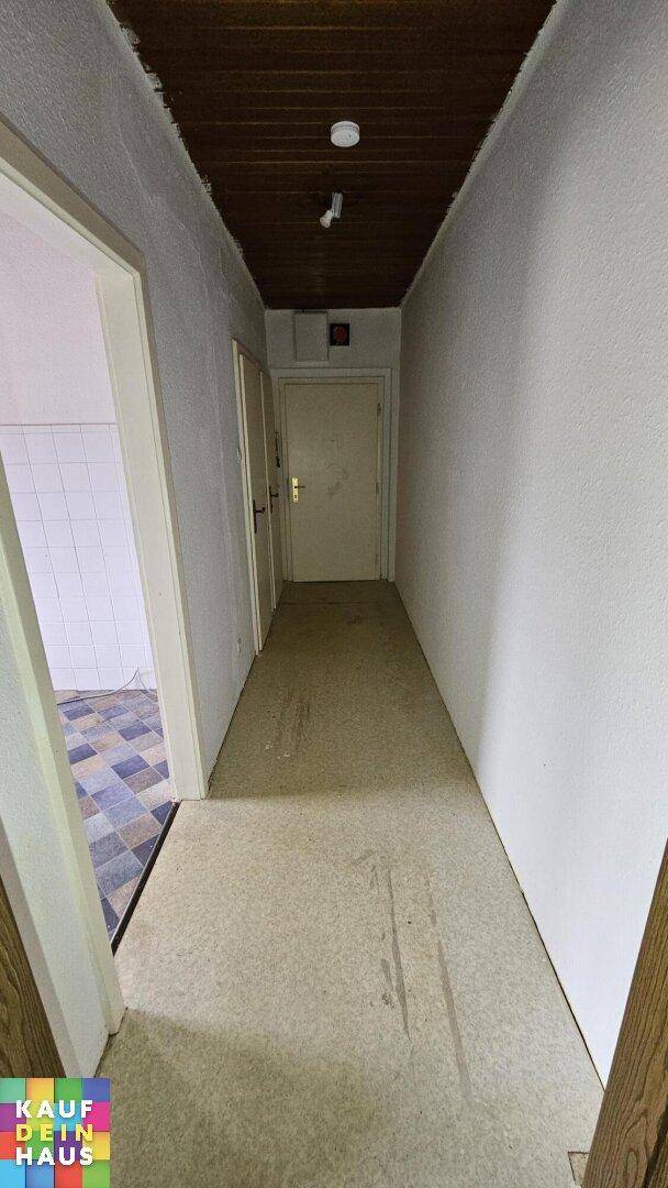 Langer Flur mit dunkler Holzdecke und Teppichboden, führt zu mehreren Türen.