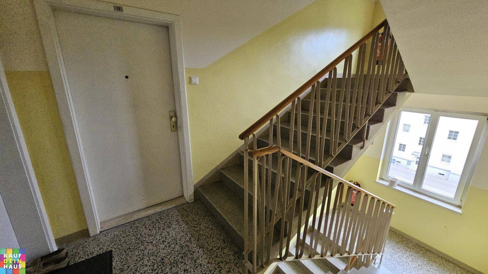 Treppenhaus mit gelben Wänden und robustem Geländer, führt zu den oberen Etagen.