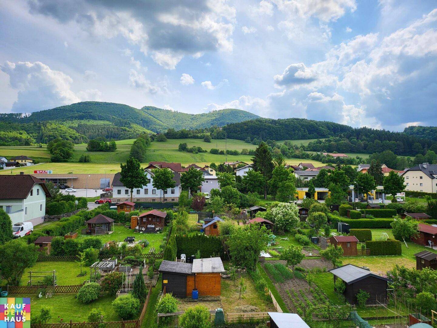 Weitläufiger Blick über eine ländliche Siedlung mit Gärten und grünen Hügeln.