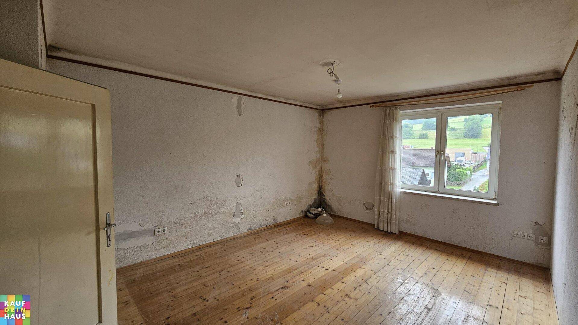 Leerer Raum mit Holzdielenboden und einem Fenster mit Blick auf die Landschaft.