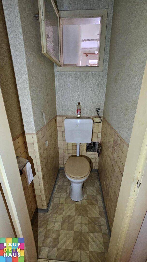 Kleines WC mit Toilette, halbhoch gefliesten Wänden und einem kleinen Fenster.