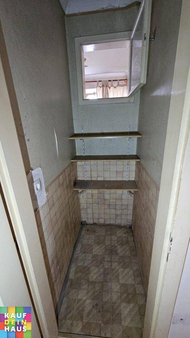 Kleiner Abstellraum mit Regalen, gefliesten Wänden und einem kleinen Fenster.