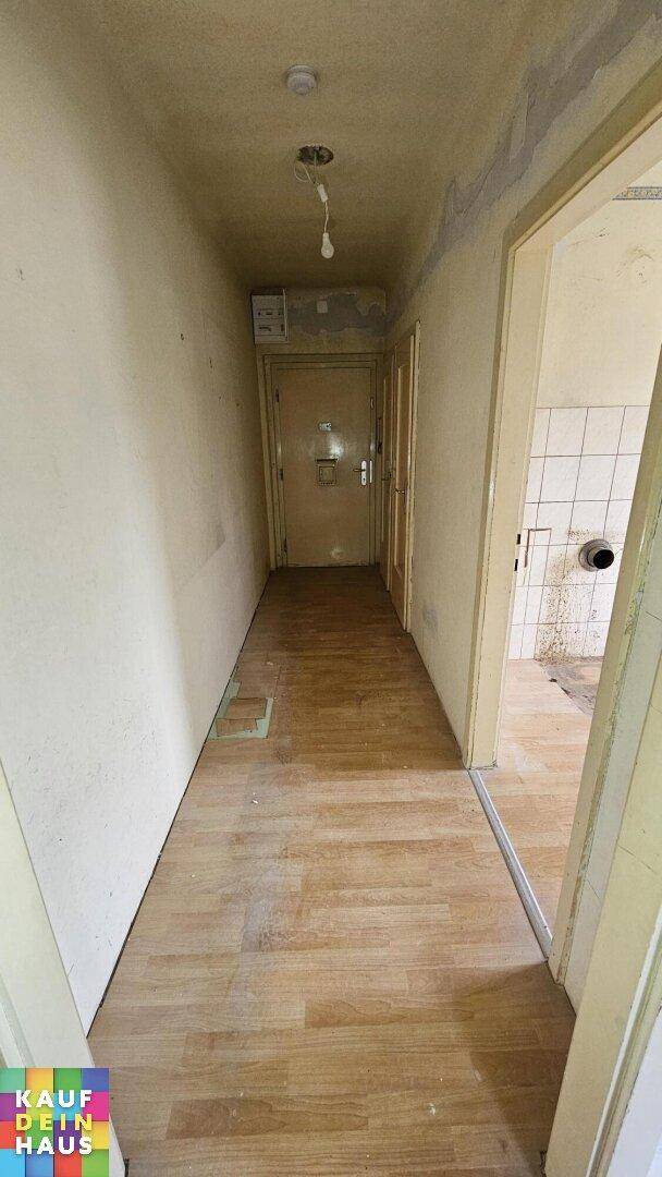Langer Flur mit Holzdielenboden und mehreren Türen, der Renovierungsbedarf zeigt.