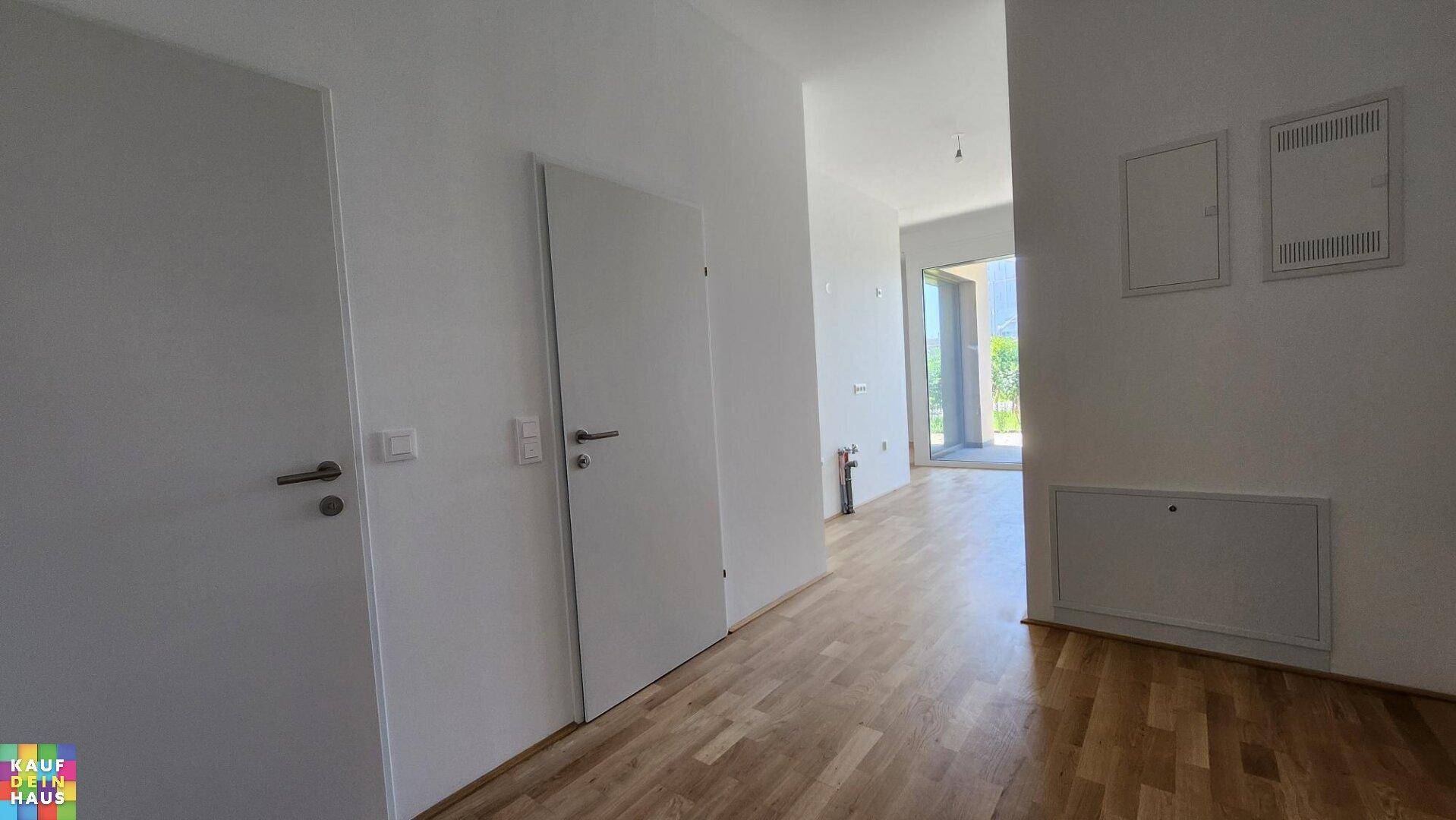 Heller Flur mit Holzboden und weißen Türen, der zu einem lichtdurchfluteten Raum führt.