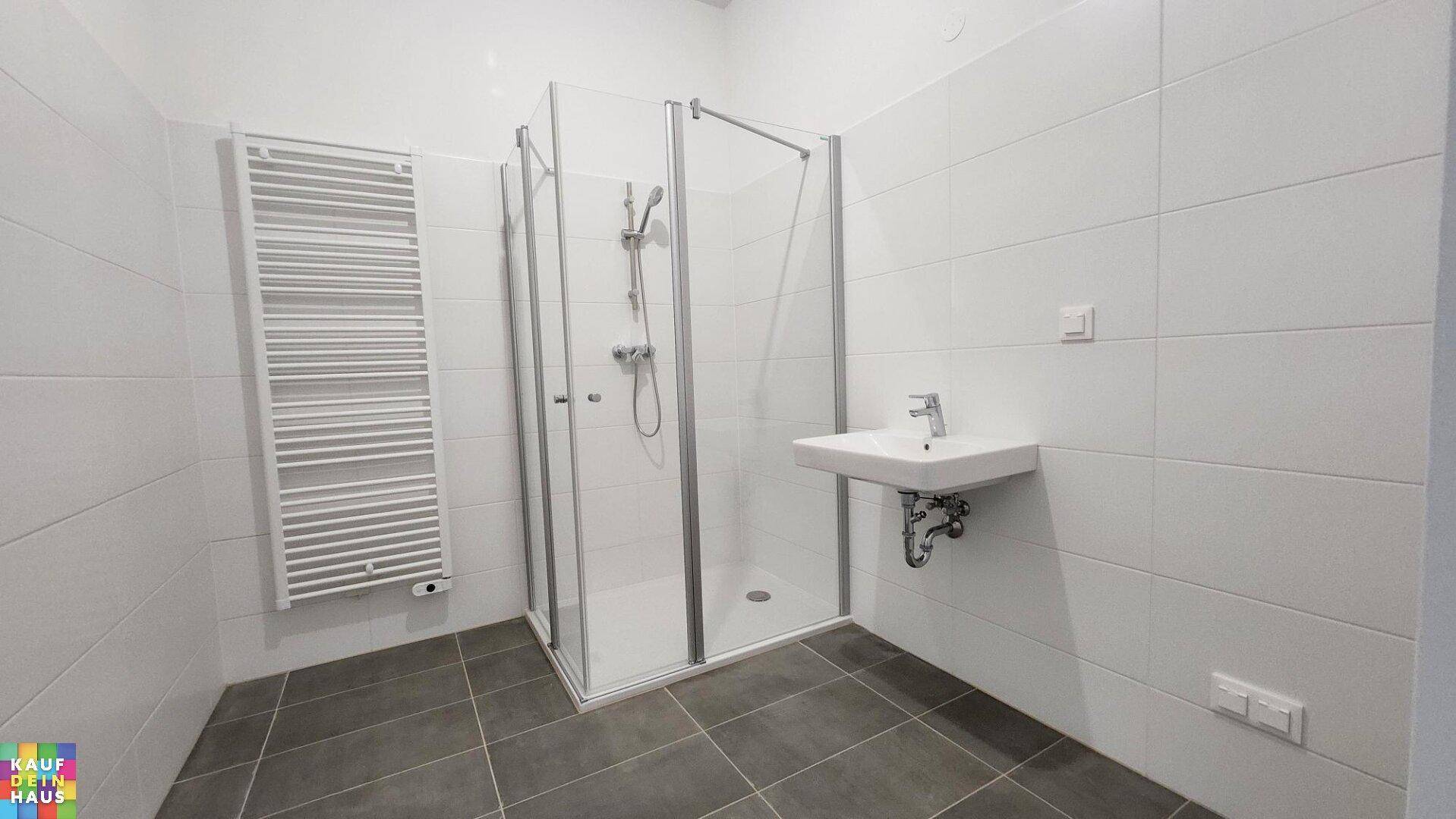 Modernes Badezimmer mit Duschkabine, Waschbecken und beheiztem Handtuchhalter.