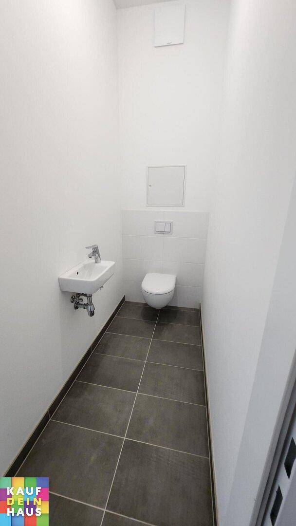 Modernes Gäste-WC mit dunklen Fliesen, wandhängender Toilette und kleinem Waschbecken.