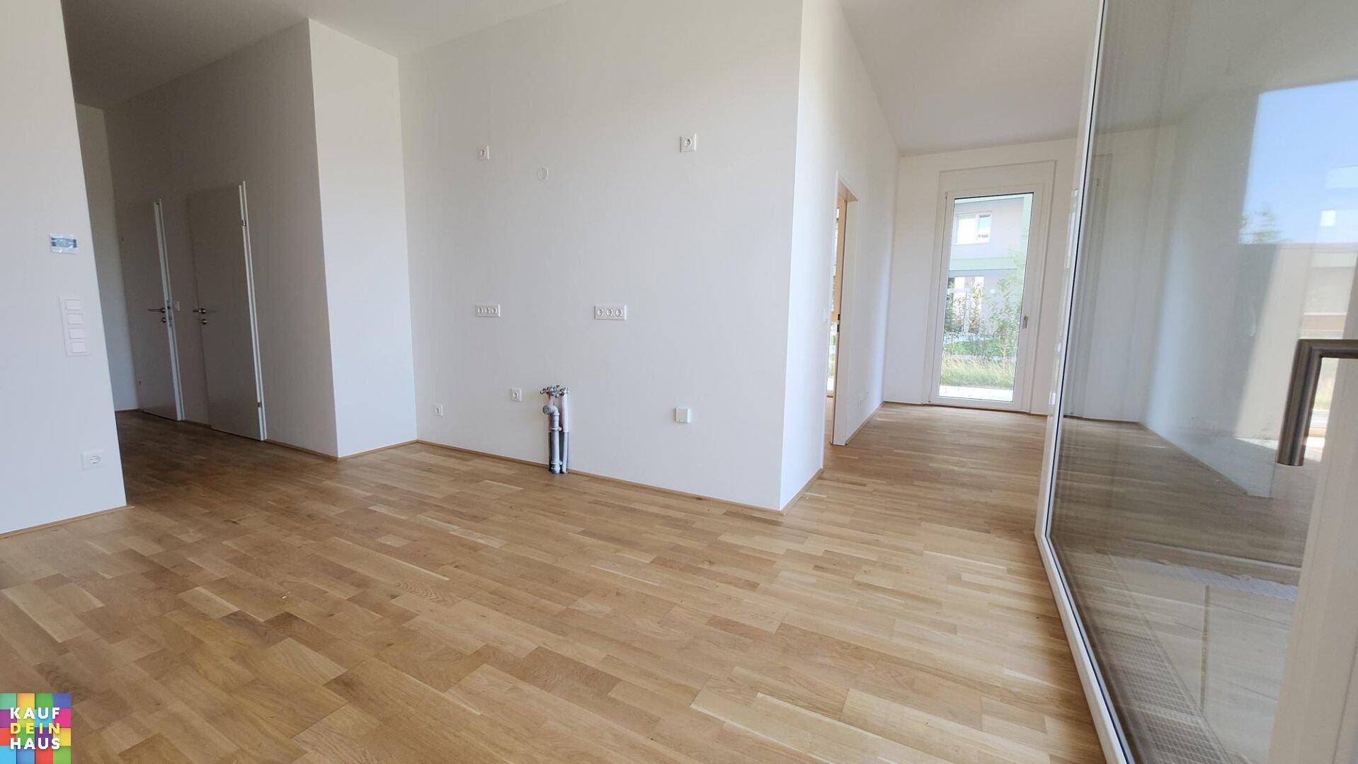 Offener Wohnbereich mit hellem Holzboden und viel Tageslicht durch große Fenster.