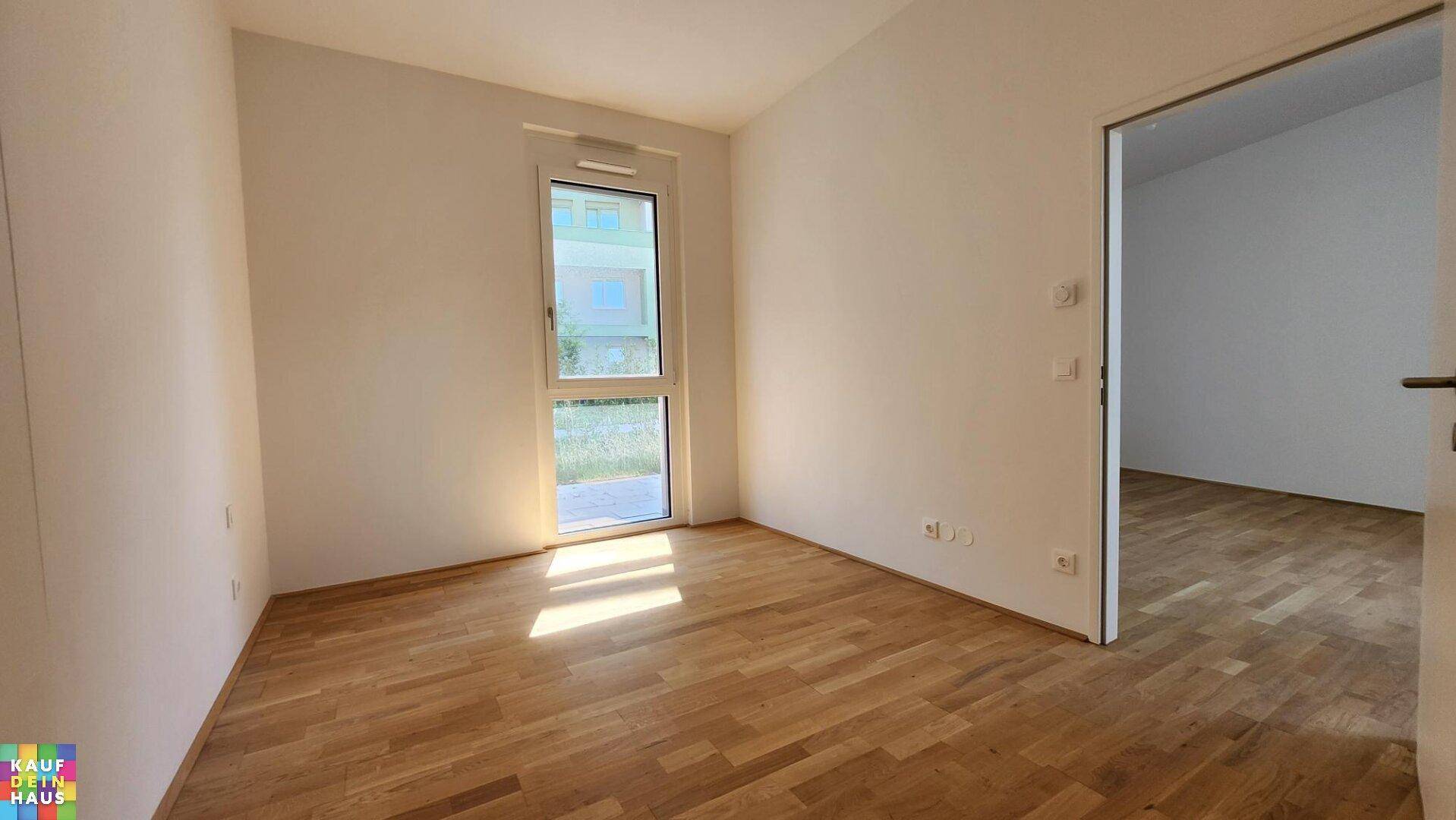 Lichtdurchflutetes Schlafzimmer mit Holzboden und Fenster mit Blick ins Grüne.