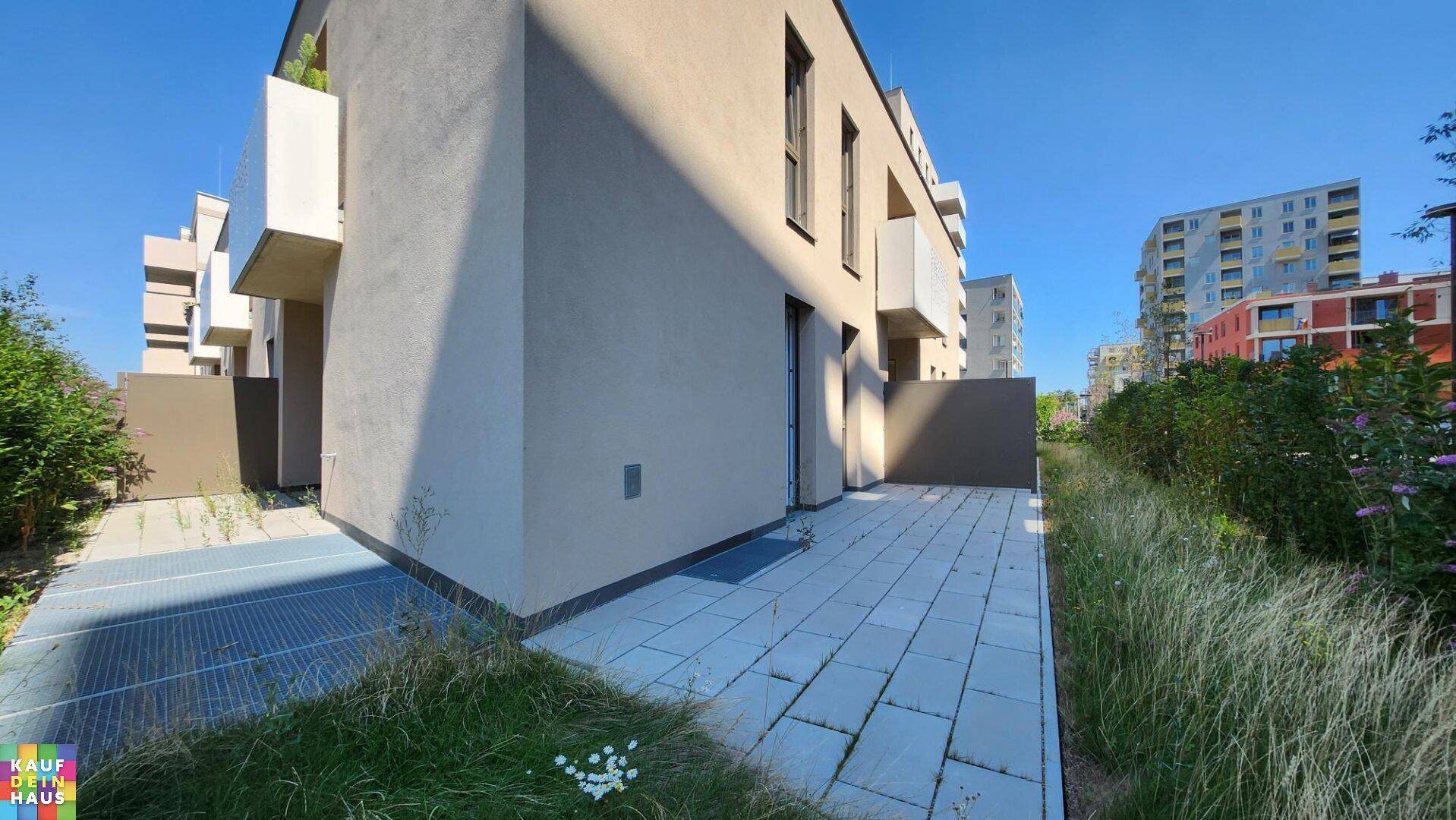 Moderne Gebäudefassade mit gepflasterter Terrasse und begrüntem Außenbereich.
