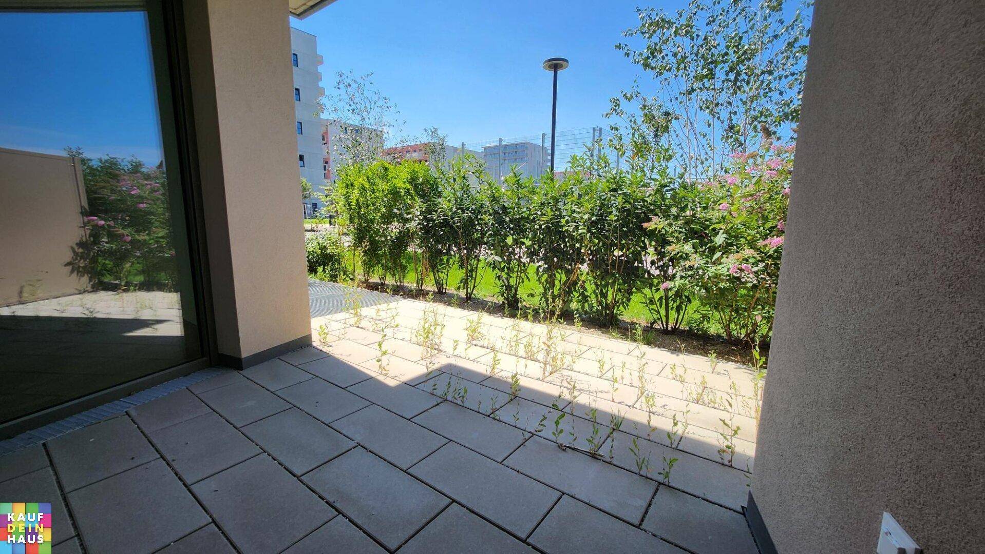 Sonniger Terrassenbereich mit gepflastertem Boden und einer grünen Hecke als Abgrenzung.