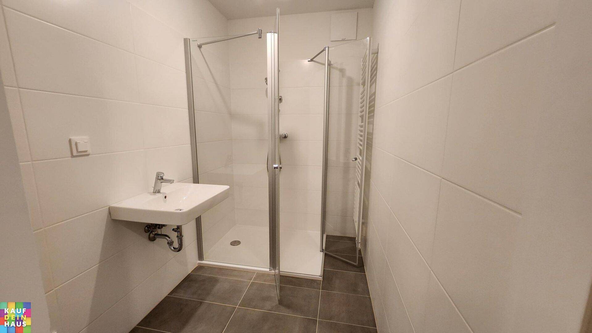 Modernes Badezimmer mit Duschkabine, Waschbecken, weißen Wandfliesen und Handtuchheizkörper.