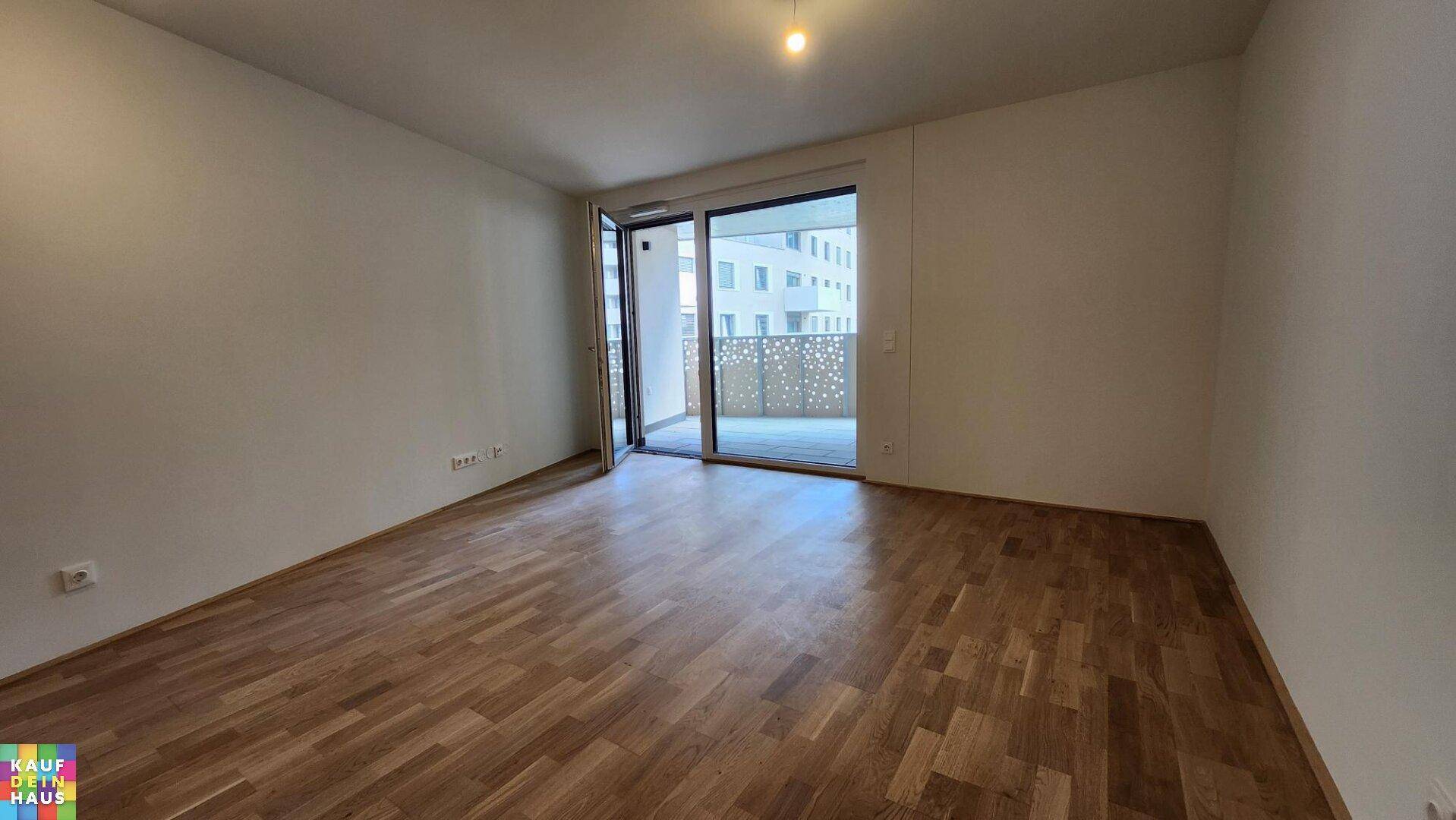 Geräumiges Wohnzimmer mit Parkettboden, weißen Wänden und großem Balkonzugang.
