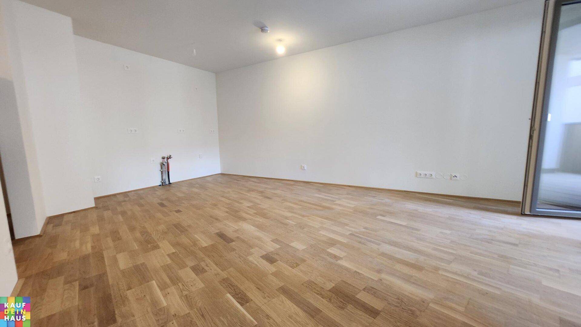 Leerer Küchenbereich mit Parkettboden, weißen Wänden und Anschlüssen für eine Einbauküche.