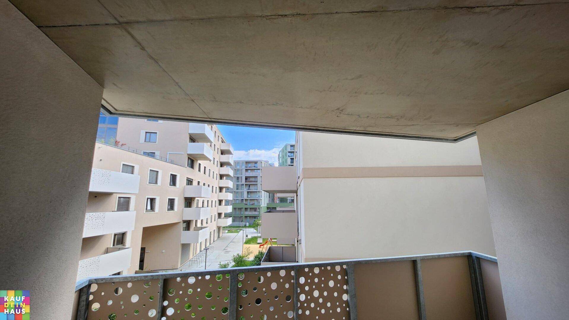 Blick vom Balkon auf die moderne Architektur der umliegenden Wohngebäude unter blauem Himmel.
