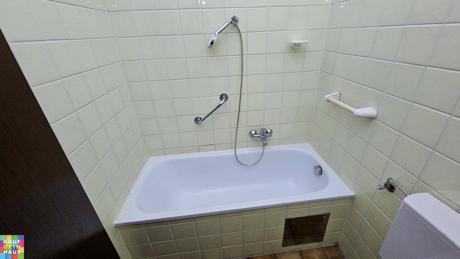 Badezimmer mit Badewanne, Duschvorrichtung und Haltegriffen an den Wänden.