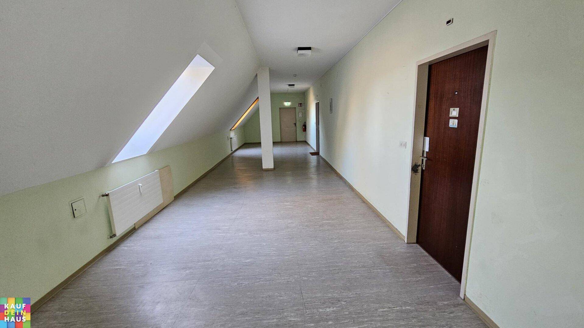 Langer Flur mit hellem Boden, schrägen Wänden und Dachfenstern für natürliches Licht.