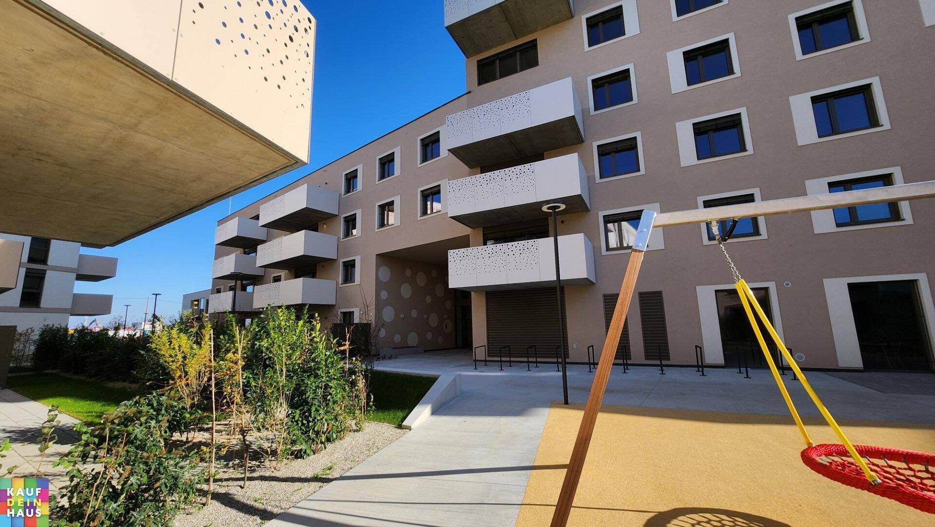 Moderner Wohnkomplex mit einem Spielplatz im Freien und Balkonen an der Fassade.
