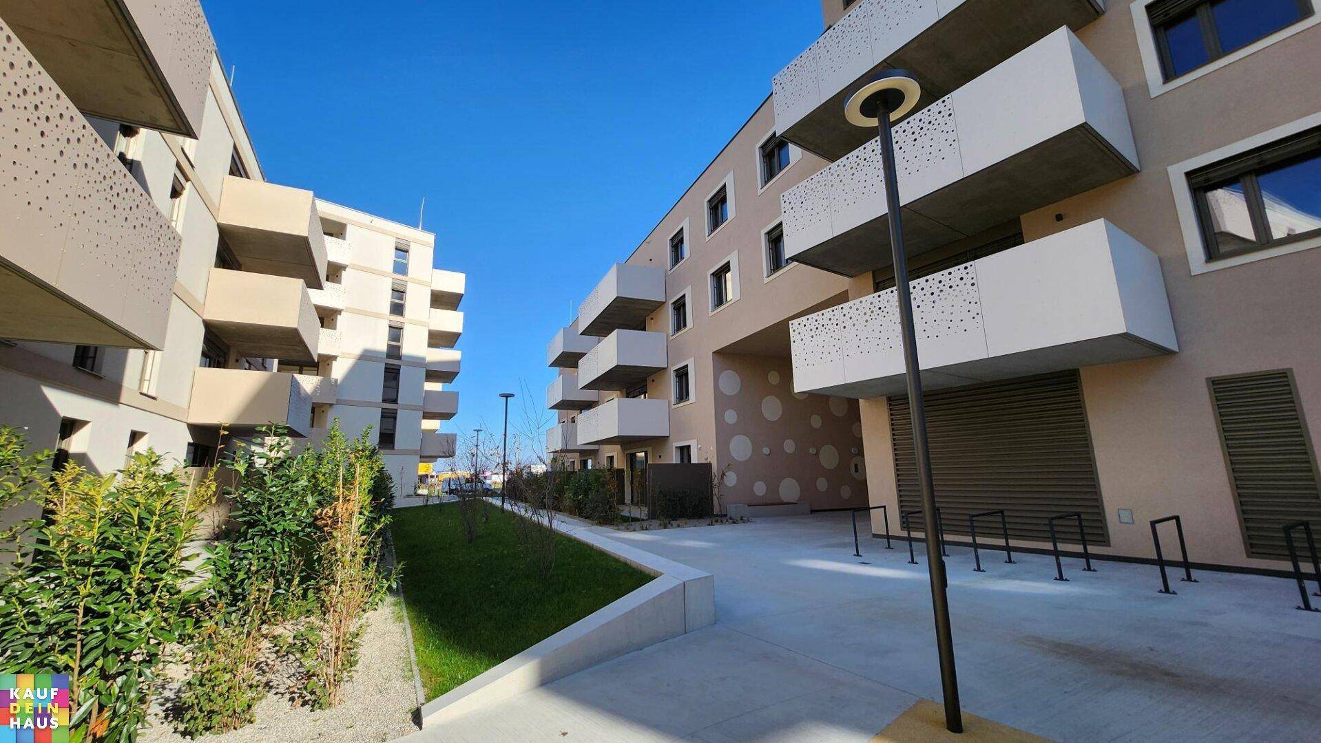 Ansicht des modernen Wohngebäudes mit perforierten Balkonbrüstungen und gepflasterten Wegen.