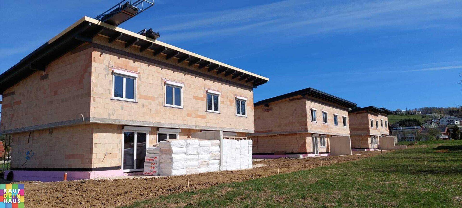Reihe von im Bau befindlichen Doppelhäusern mit sichtbaren Rohbauelementen und Fenstern.