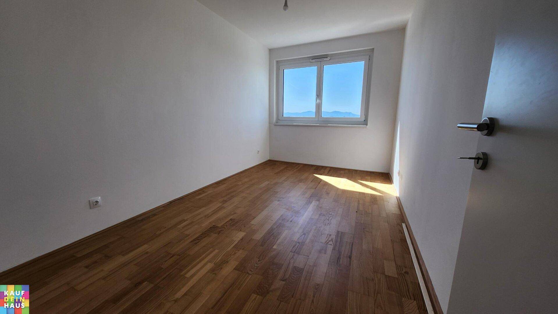 Helles, leeres Zimmer mit Parkettboden und einem Fenster, das einen weiten Blick bietet.