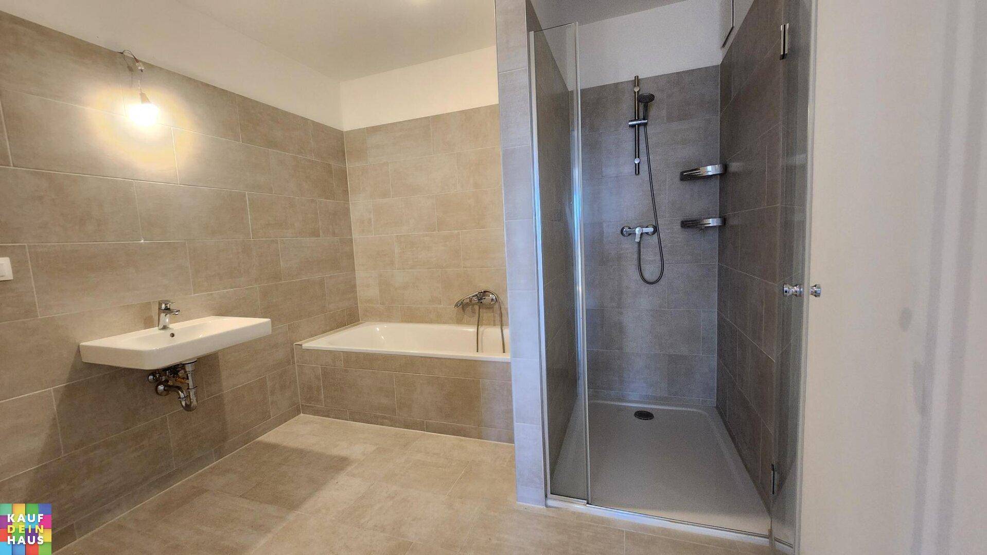 Geräumiges Badezimmer mit Badewanne, Duschkabine, Waschbecken und beigefarbenen Wandfliesen.