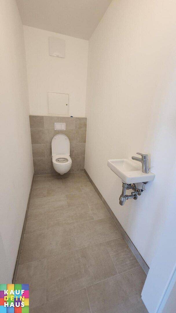 Modernes Gäste-WC mit Wand-WC, kleinem Waschbecken und hellgrauen Fliesen.