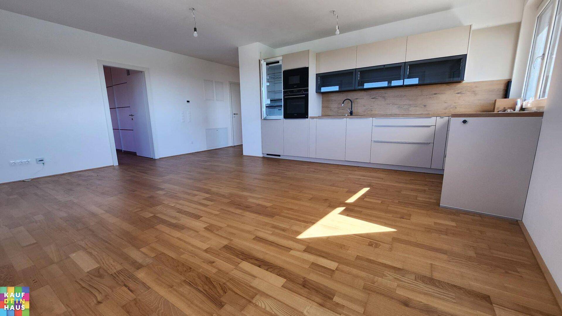 Moderne Einbauküche mit hellen Schränken, Holztheke und integrierten Geräten in offenem Wohnbereich.