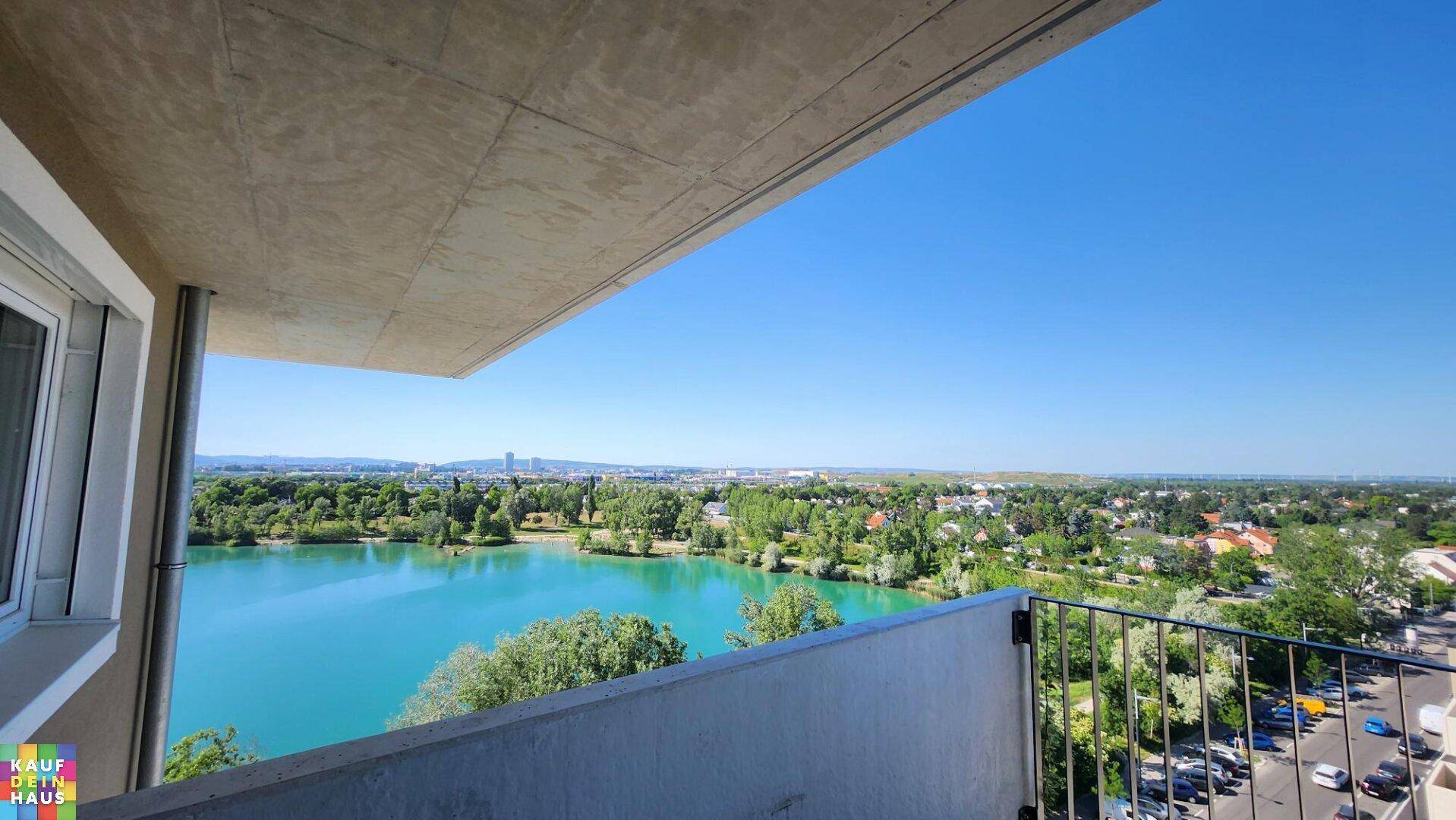 Balkon mit weitem Blick über einen See, die Stadt und grüne Bäume unter strahlend blauem Himmel.