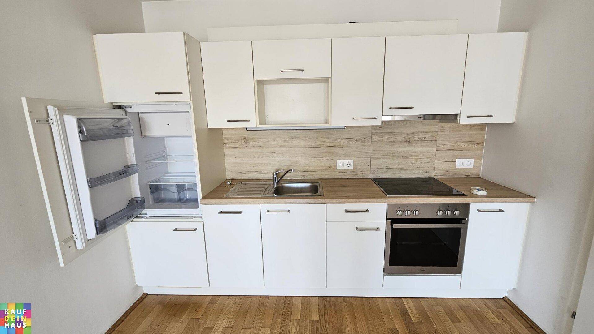 Kompakte Einbauküche mit weißen Schränken, Kühlschrank und Kochfeld.