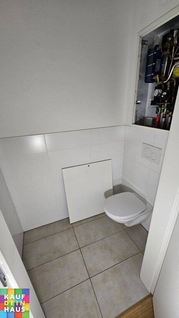 Separate Toilette mit Wand-WC und Fliesenboden, daneben ein Wartungsschacht.