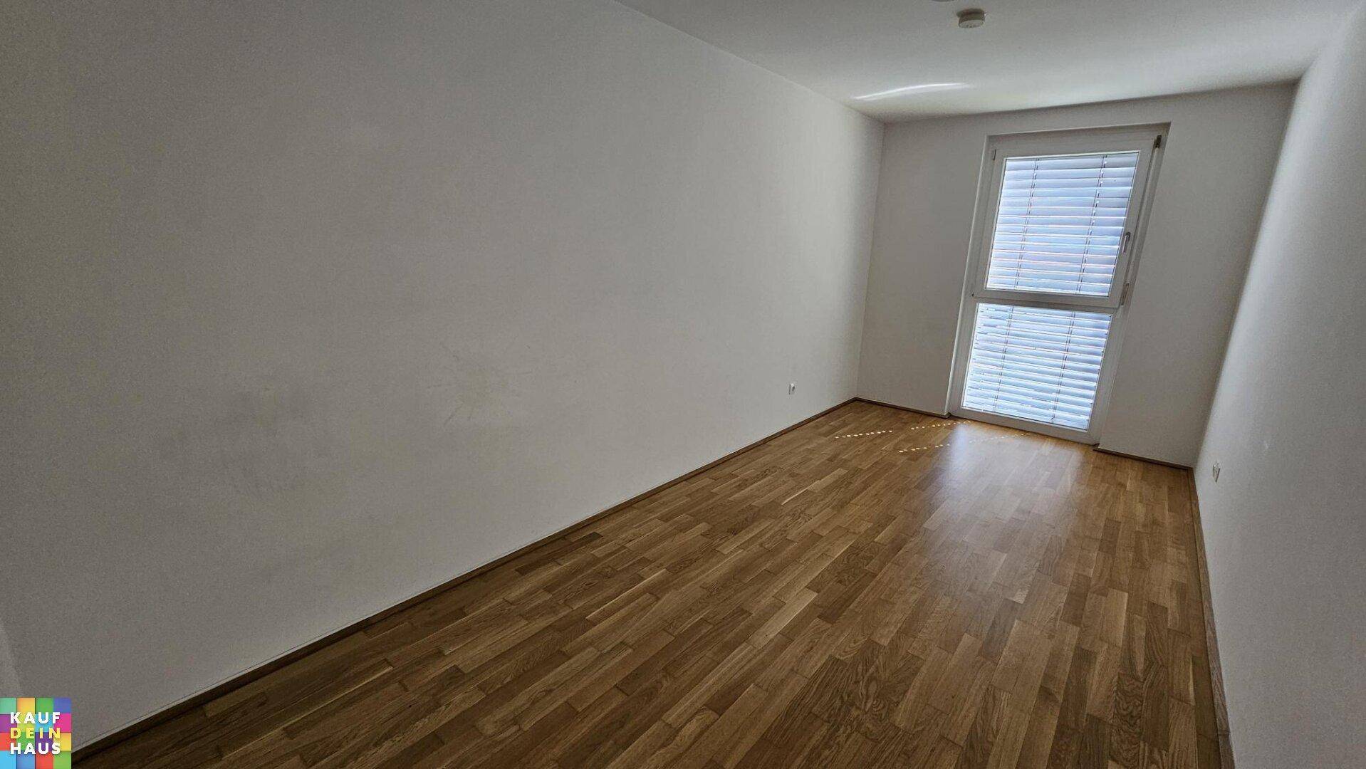 Leeres Zimmer mit Parkettboden und großem Fenster, ideal als Schlaf- oder Arbeitszimmer.