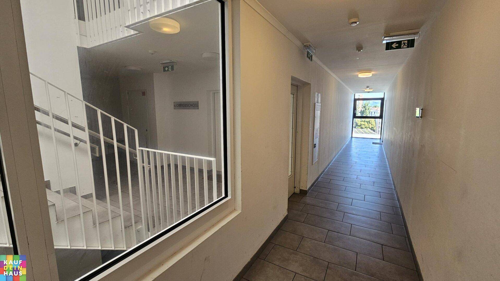 Gemeinschaftlicher Flur mit Fliesenboden und Blick auf das Treppenhaus.