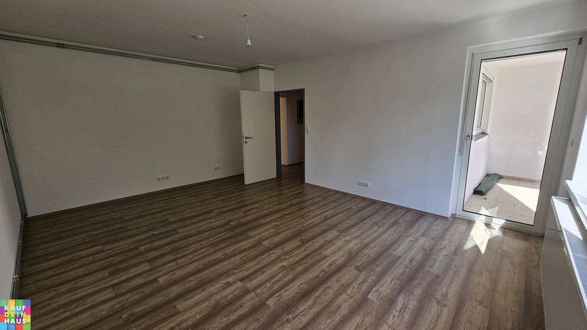 Geräumiges Wohnzimmer mit Laminatboden, weißen Wänden und direktem Zugang zum Balkon.