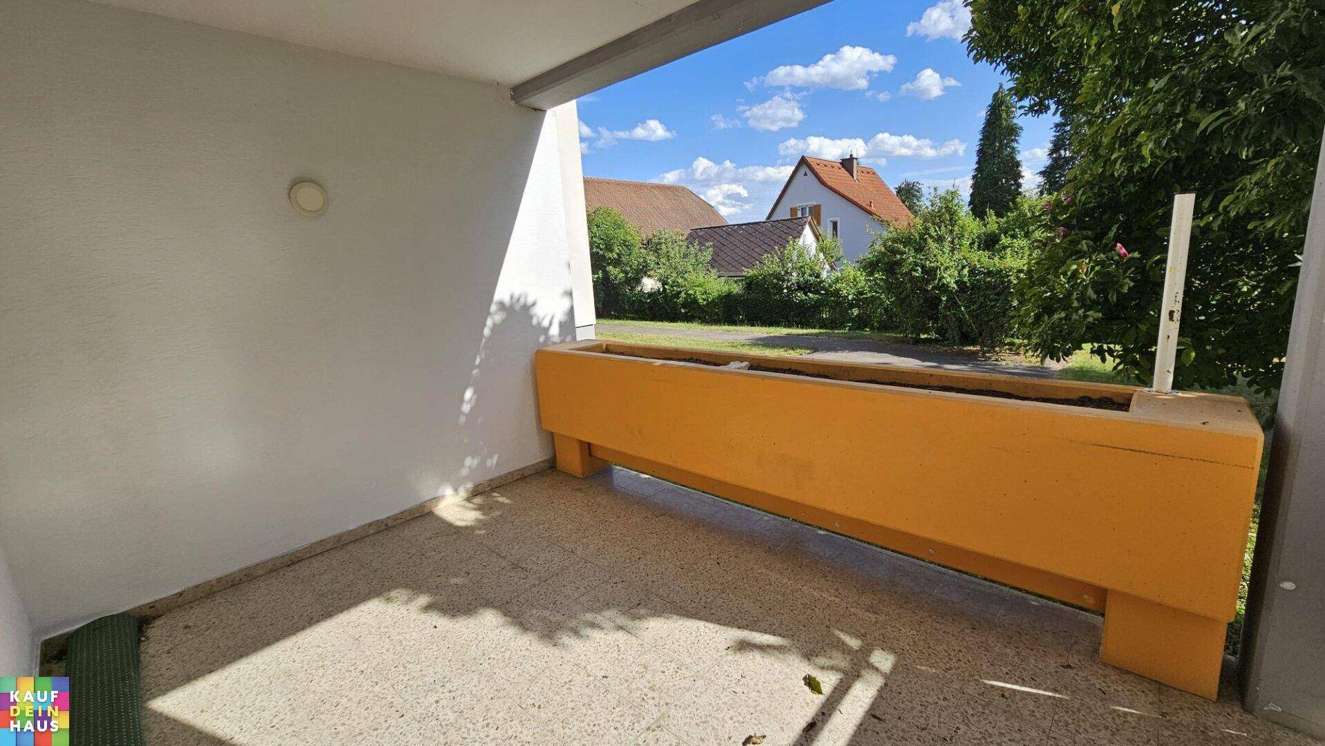 Heller Balkon mit Blumenkasten und Ausblick auf die umliegenden Häuser und viel Grün.
