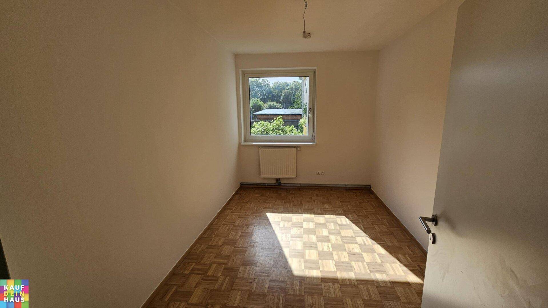 Sonniger Raum mit klassischem Parkettboden und einem Fenster, das viel Tageslicht hereinlässt.