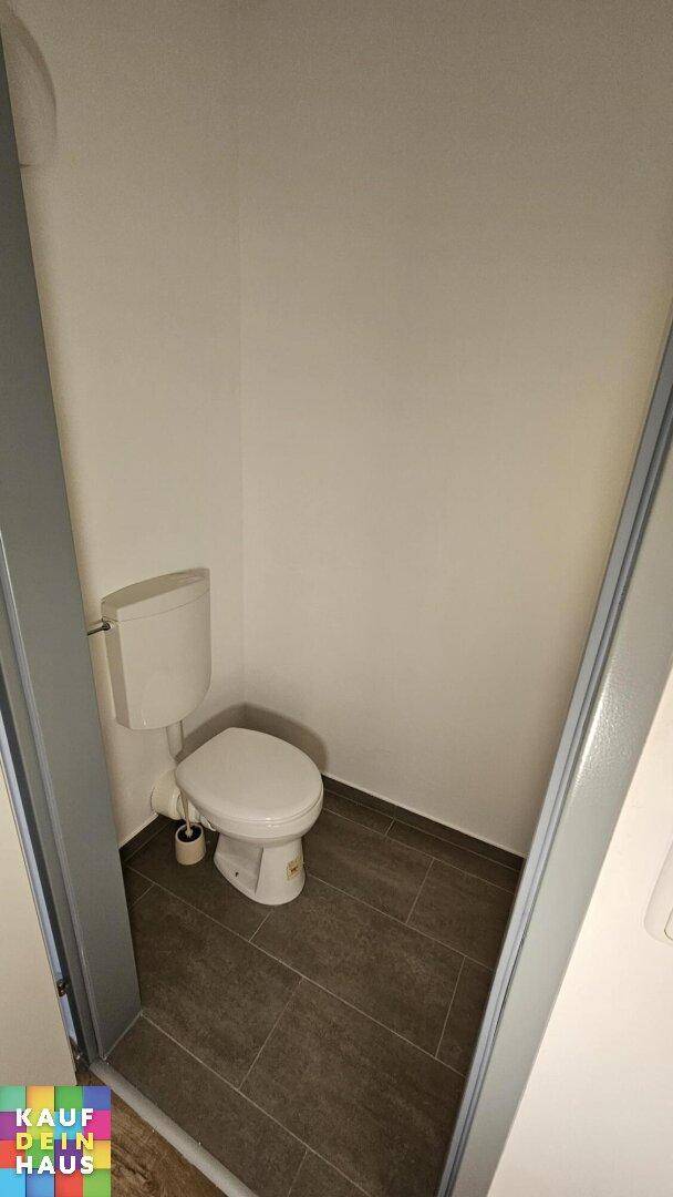 Separates Gäste-WC mit dunklen Bodenfliesen und einer einfachen Toilette.