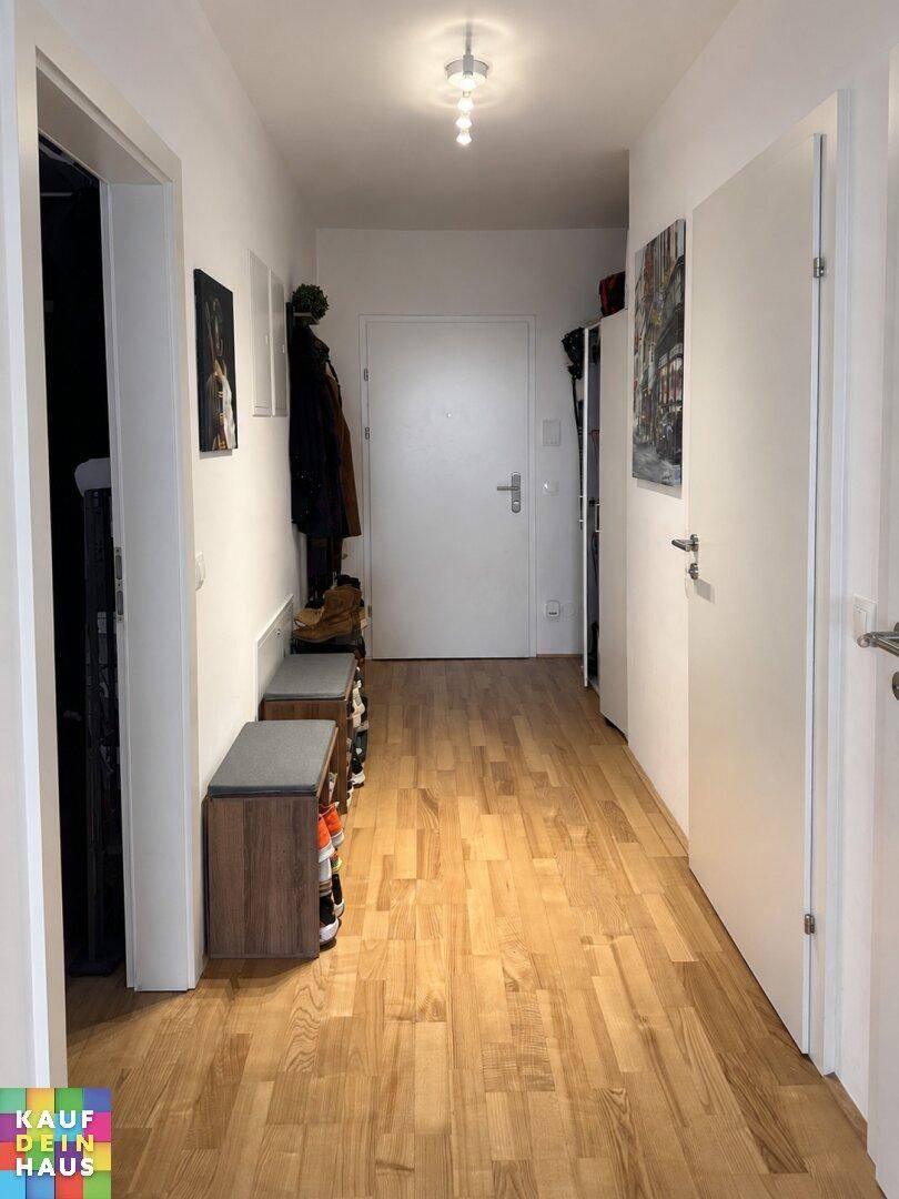 Heller Flur mit Holzboden, weißen Wänden und mehreren Türen, die zu den Zimmern führen.