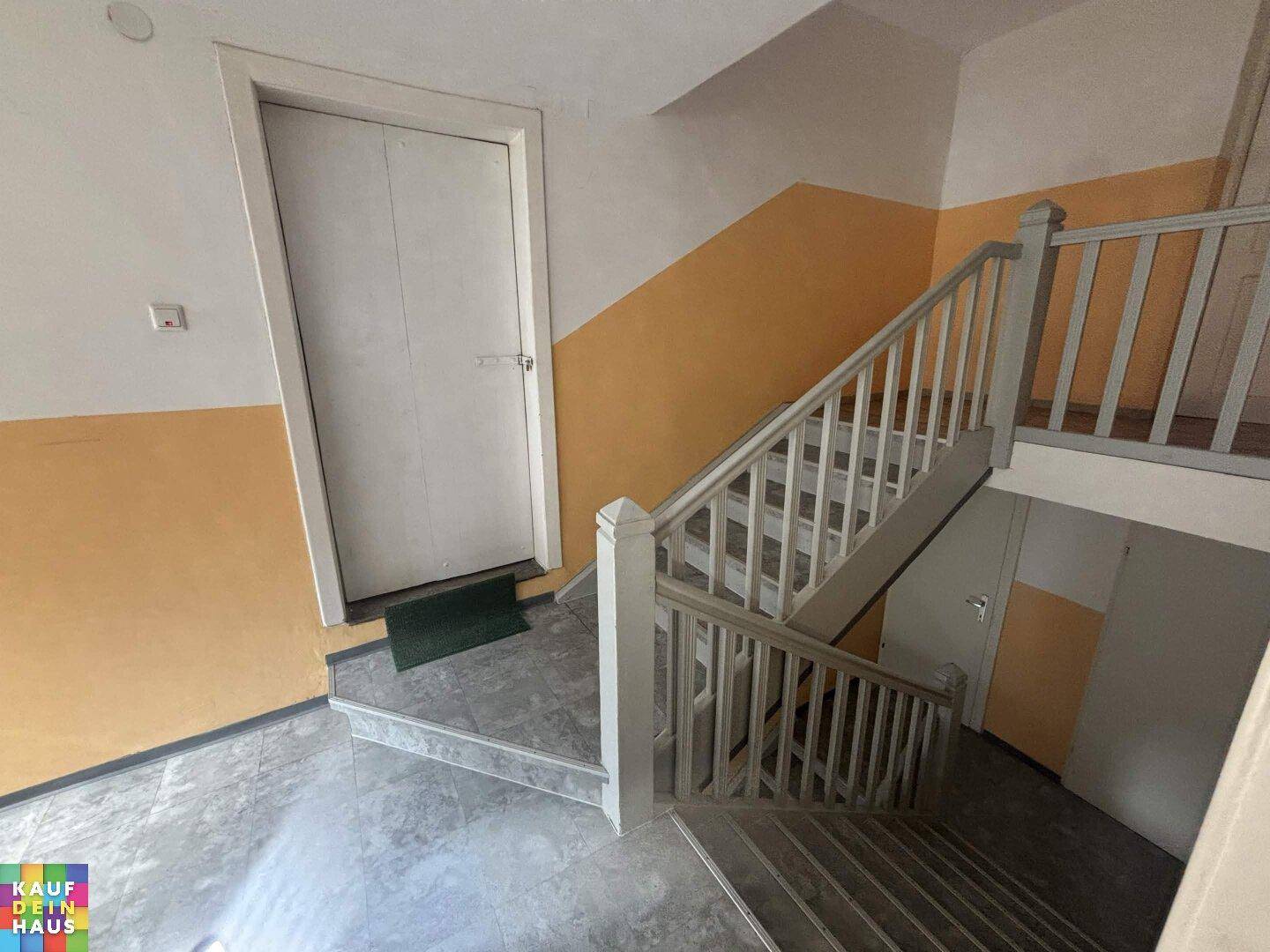Treppenhaus mit farbigen Wänden und Fliesenboden, führt zu den oberen Etagen.