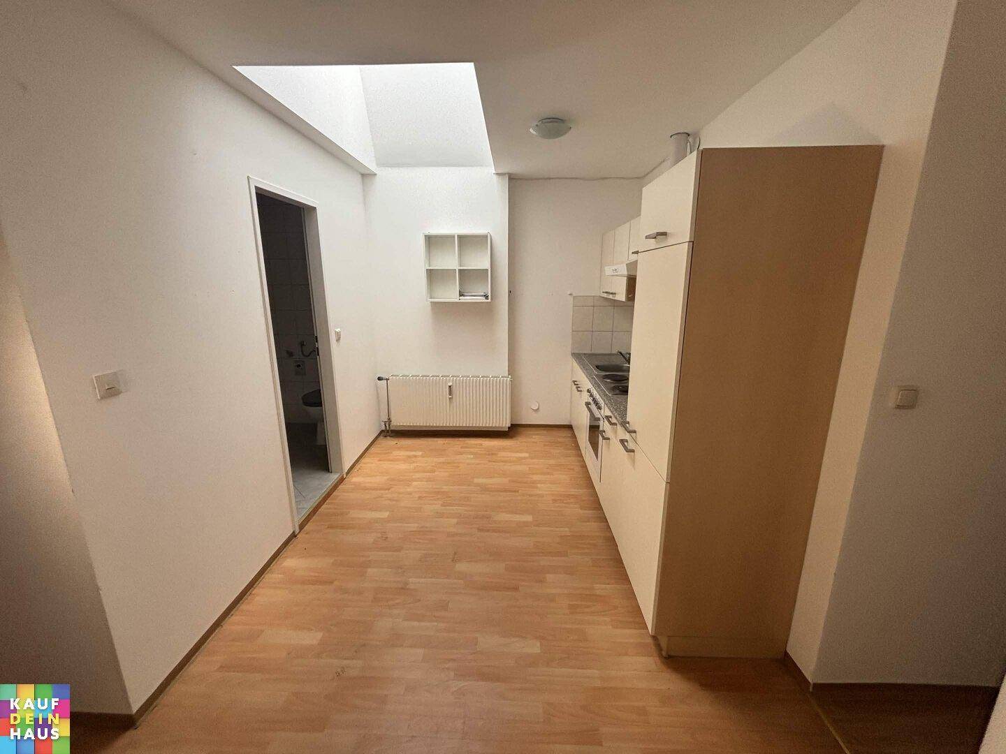 Kleine Küchenzeile mit Dachfenster und Laminatboden, ideal für eine Singlewohnung.