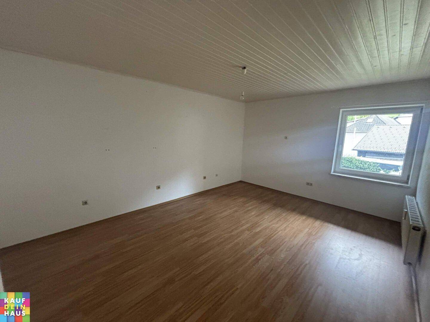 Geräumiges Zimmer mit Holzdecke, Fenster und Laminatboden, hell und einladend.