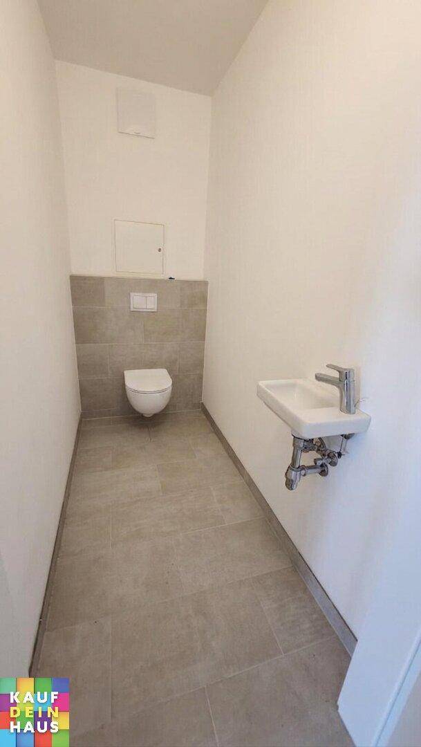 Modernes Gäste-WC mit Wand-WC, kleinem Waschbecken und hellen Fliesen in sehr gutem Zustand.