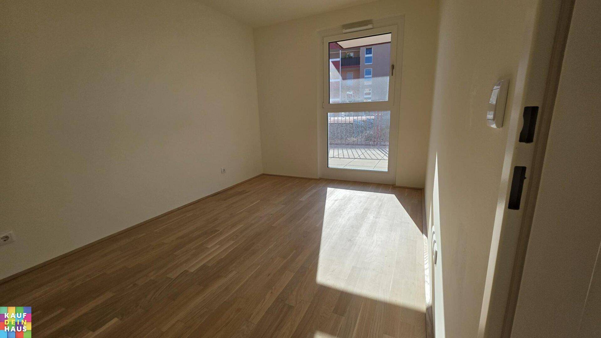 Helles Schlafzimmer mit Parkettboden und Fenster mit Blick auf die umliegenden Gebäude.