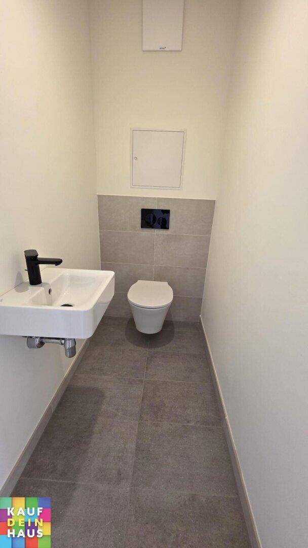 Funktionelles Gäste-WC mit wandhängender Toilette, kleinem Waschbecken und modernen Fliesen.