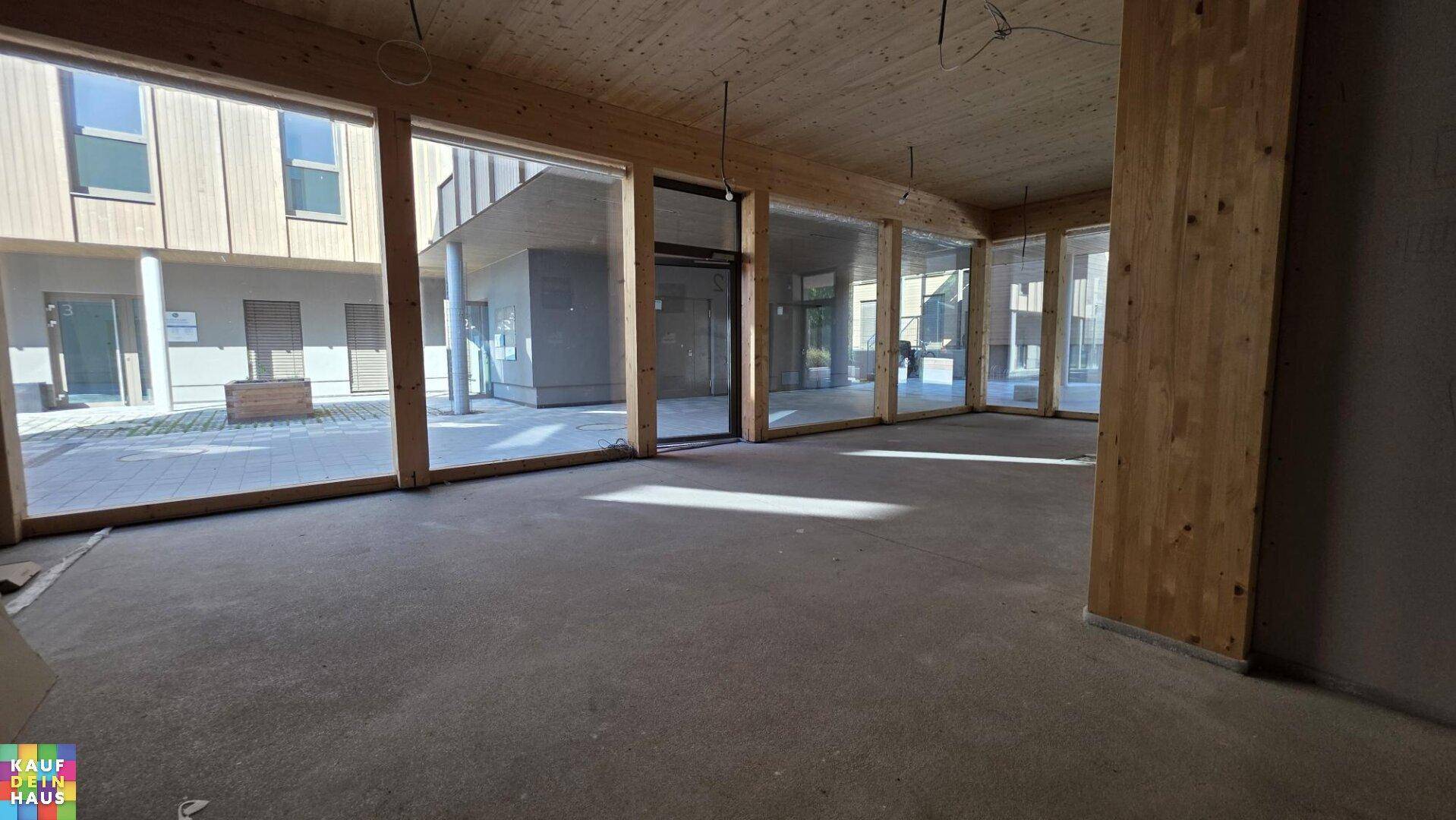 Heller, offener Raum im Rohbau mit vielen großen Fenstern, die einen Blick auf den Innenhof bieten.